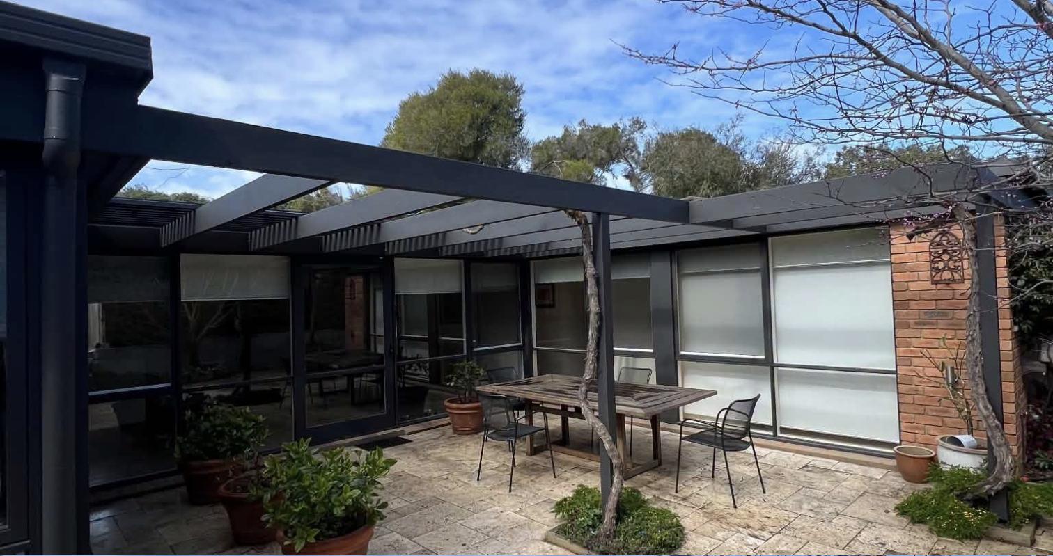Courtyard with a dark-painted pergola, glass doors, brick wall and outdoor table setting