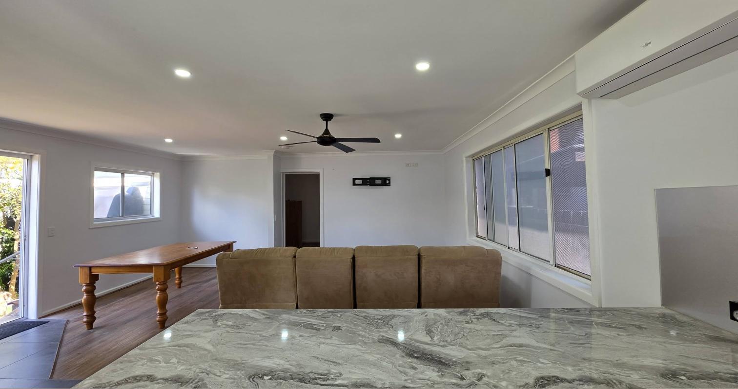 Living area after painting, with a white ceiling, light grey walls, ceiling fan and timber floors