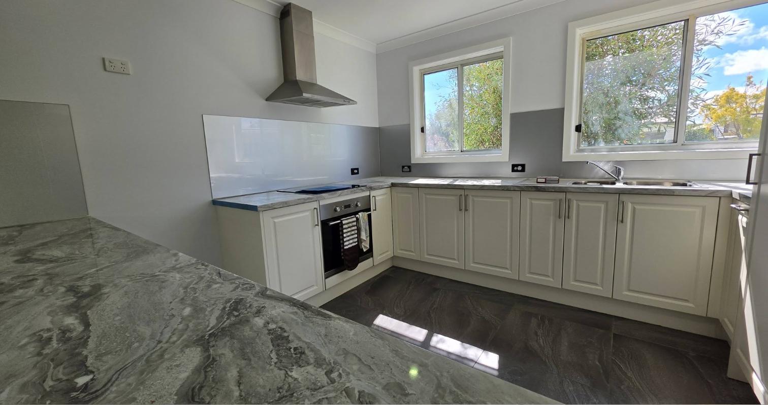 Freshly painted kitchen with white walls, cream cabinetry and a stone benchtop