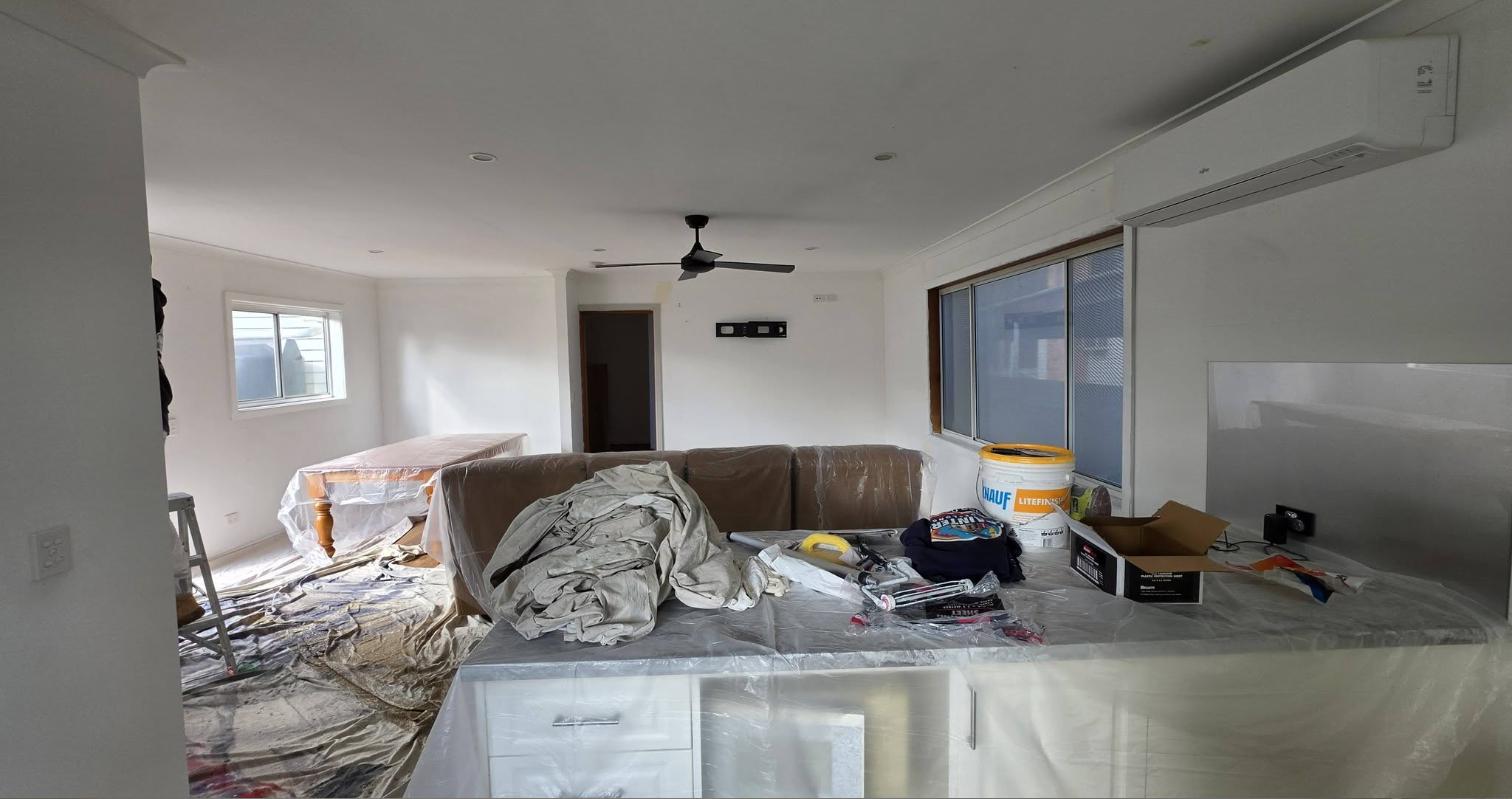 The same living area during the job, with furniture wrapped in plastic and drop sheets on the floor