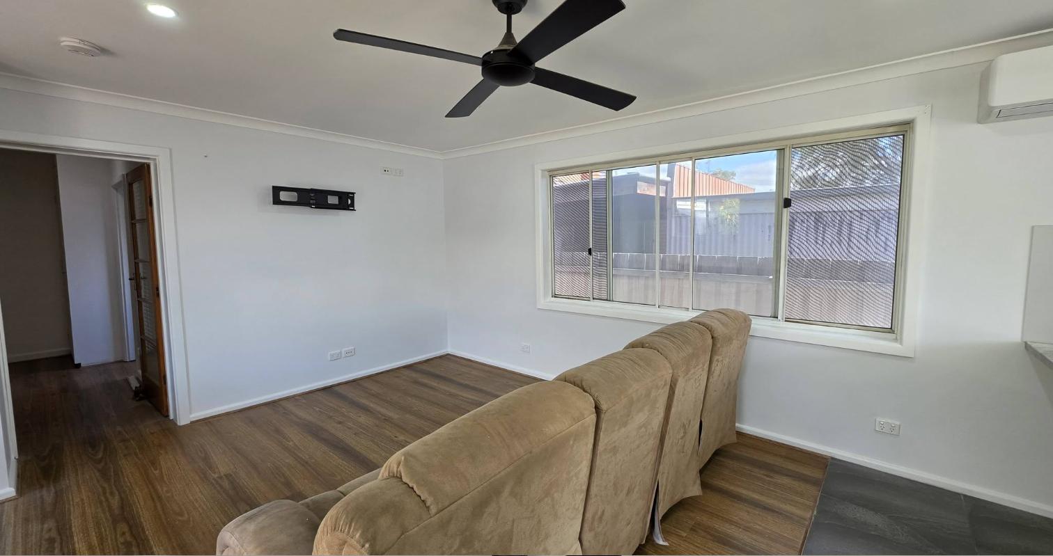 Freshly painted lounge room with white walls, timber-look floor and a ceiling fan